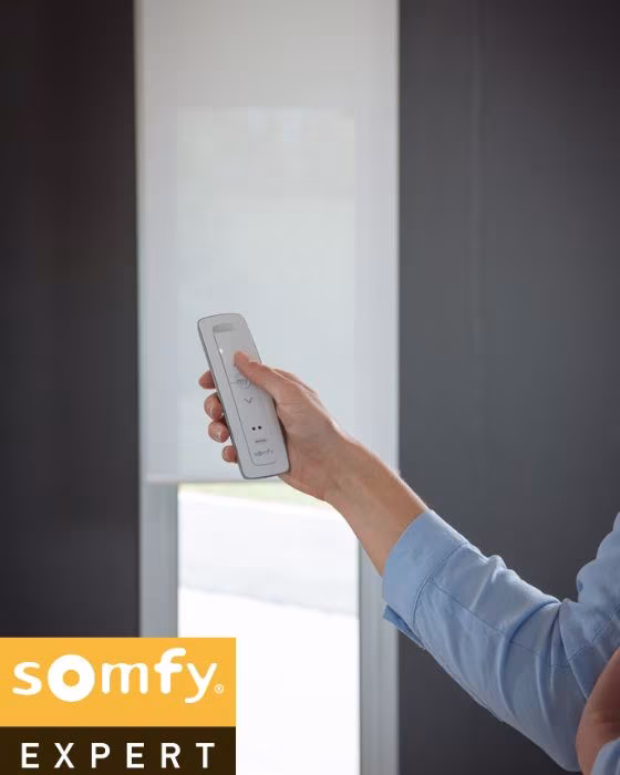 Woman controlling motorized blinds Dubai with smartphone app in modern living room with Somfy automation system